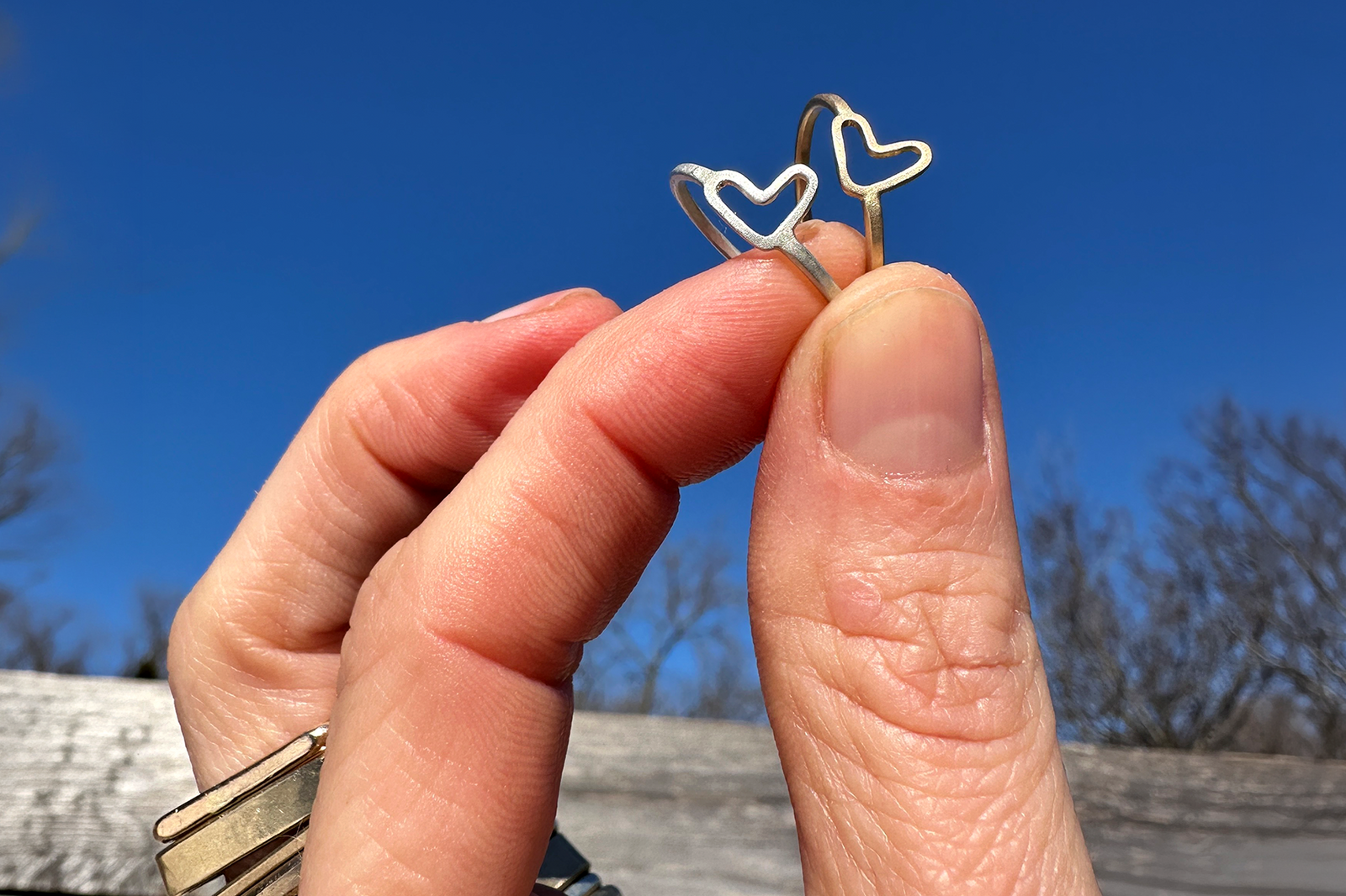 Sterling silver and gold Spread the Love heart rings held against a blue sky